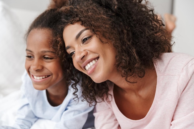 Sonriente joven madre y su pequeña hija en pijama releaxing en la cama, abrazando