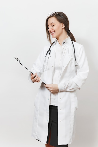 Sonriente joven médico confía en mujer con estetoscopio, gafas aisladas sobre fondo blanco. Doctora en bata médica con tarjeta sanitaria en la carpeta del bloc de notas. Concepto de medicina del personal sanitario.