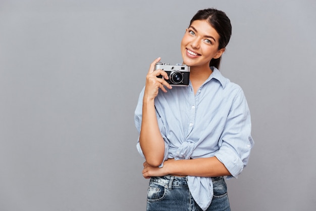 Sonriente joven morena sosteniendo foto frontal aislado en una pared gris