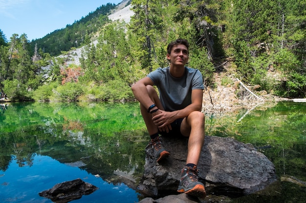 Sonriente joven muchacho adolescente caucásico relajante de un lago durante un viaje de aventura de trekking de montaña