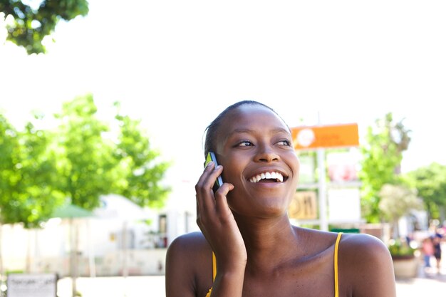 Sonriente joven mujer africana en la ciudad hablando por teléfono móvil