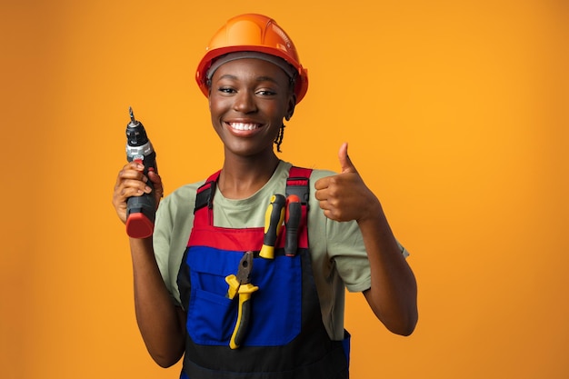 Sonriente joven mujer afroamericana en casco con herramienta de destornillador en estudio