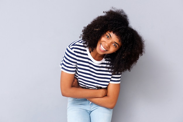 Sonriente joven mujer afroamericana contra el fondo gris con los brazos cruzados