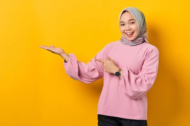 Sonriente joven mujer asiática en camisa rosa mostrando espacio de copia en la palma sobre fondo amarillo