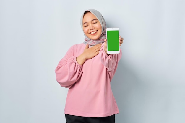 Sonriente joven mujer asiática en camisa rosa mostrando la pantalla en blanco del teléfono móvil recomendando la aplicación aislada sobre fondo blanco.