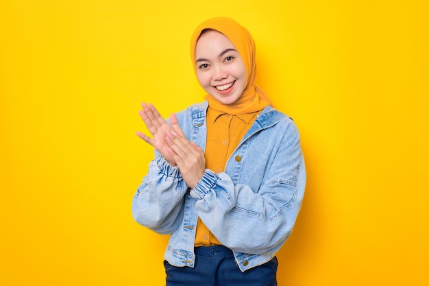 Sonriente joven mujer asiática en chaqueta de jeans aplaudiendo celebrando el éxito felicitando a alguien aislado sobre fondo amarillo