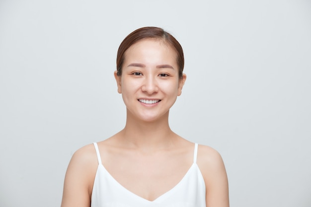 Sonriente de joven mujer asiática sin maquillaje sobre fondo blanco.