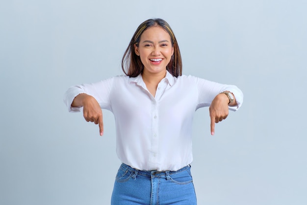 Foto sonriente joven mujer asiática señalando con el dedo hacia abajo invitando a la gente a seguir aislado sobre fondo blanco.