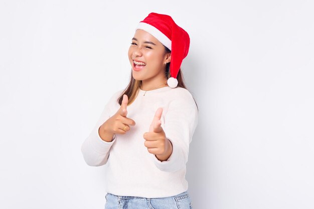 Sonriente joven mujer asiática en sombrero de Navidad señalando con el dedo a la cámara aislada sobre fondo blanco celebración de vacaciones de Navidad y concepto de Año Nuevo