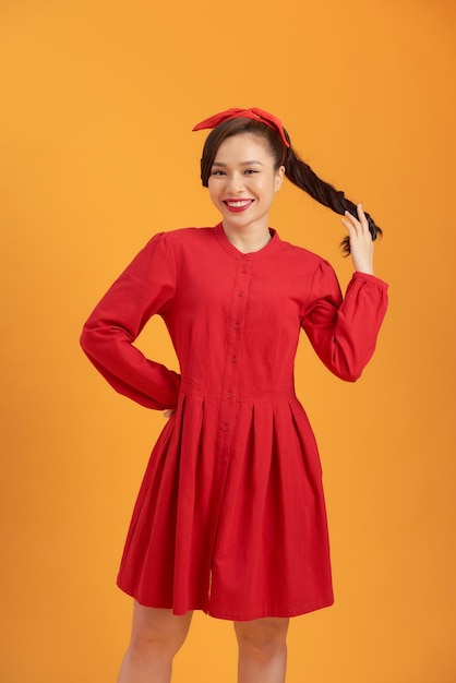 Sonriente joven mujer asiática vistiendo vestido rojo aislado sobre fondo naranja