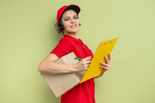 Sonriente joven mujer bonita entrega con caja de cartón y portapapeles