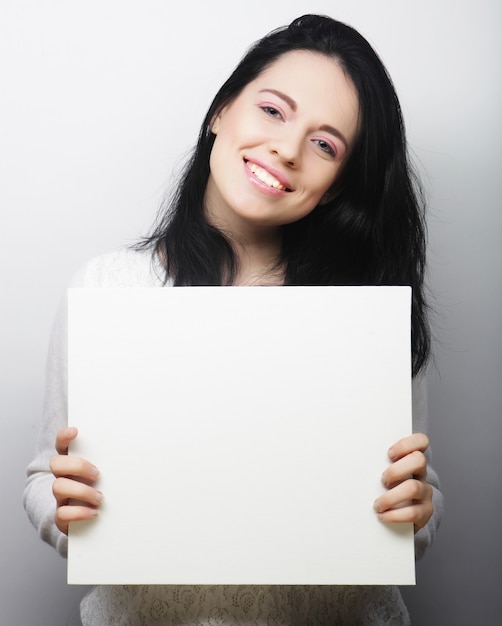 Sonriente joven mujer de estilo casual mostrando letrero en blanco, sobre fondo gris aislado