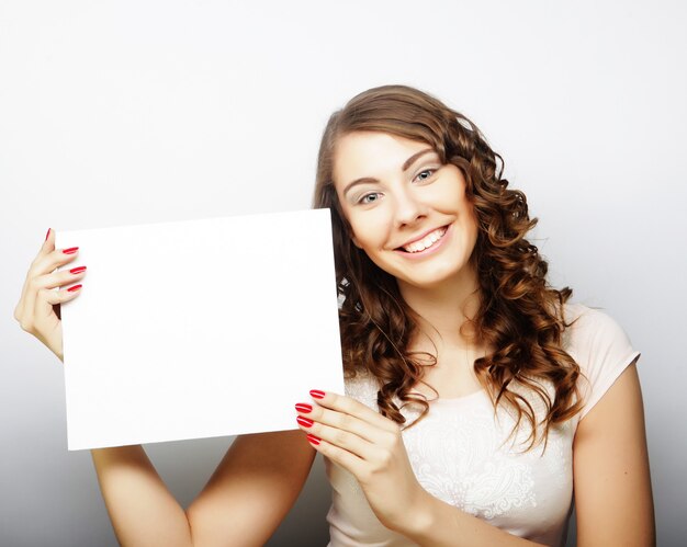 Sonriente joven mujer de estilo casual mostrando letrero en blanco, sobre fondo gris aislado