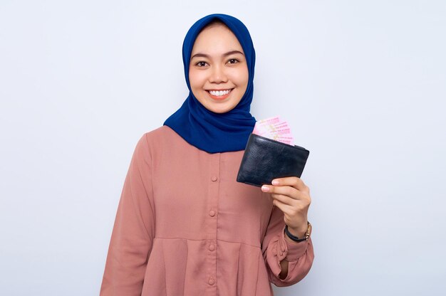 Sonriente joven mujer musulmana asiática en camisa rosa mostrando billetera llena de billetes de dinero aislado sobre fondo blanco Concepto de estilo de vida de la gente