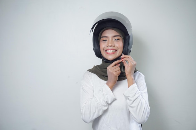 Sonriente joven mujer musulmana asiática con casco de motocicleta aislado sobre fondo blanco.