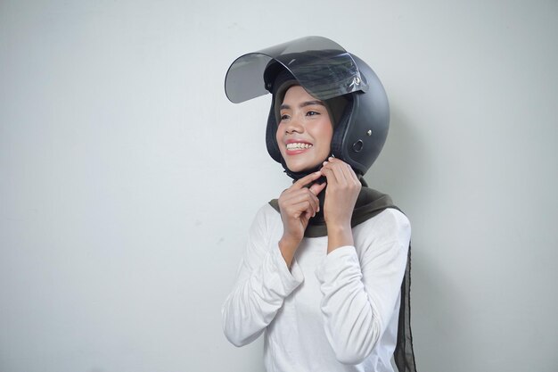 Sonriente joven mujer musulmana asiática con casco de motocicleta aislado sobre fondo blanco.