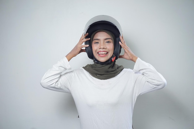 Sonriente joven mujer musulmana asiática con casco de motocicleta aislado sobre fondo blanco.
