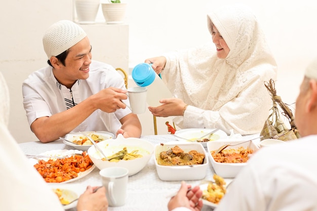 Sonriente joven mujer musulmana sirviendo agua a su hermano en el comedor durante el momento de eid mubarak