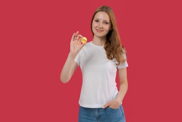 Sonriente joven mujer de negocios con camisa blanca sosteniendo bitcoin en la mano posando