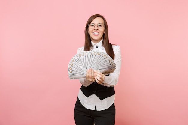 Sonriente joven mujer de negocios exitosa en vasos sosteniendo un montón de dólares, dinero en efectivo aislado sobre fondo rosa. Jefa. Concepto de riqueza de carrera de logro. Copie el espacio para publicidad.