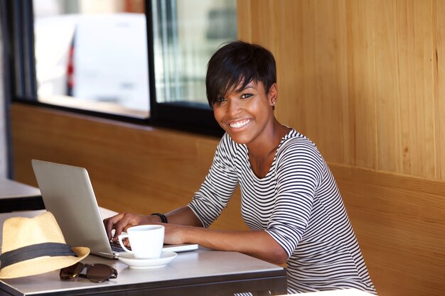 Sonriente joven mujer negra usando laptop