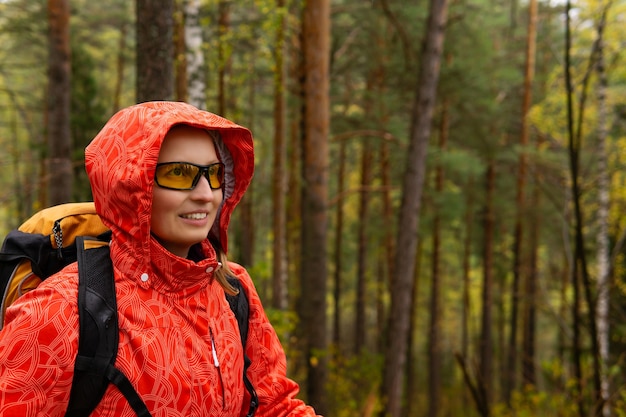 Sonriente joven mujer rubia viajero con mochila en el bosque de otoño