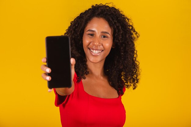 Sonriente joven mujer de Santa con sombrero de Navidad con teléfono móvil con pantalla en blanco vacía aislada sobre fondo amarillo.