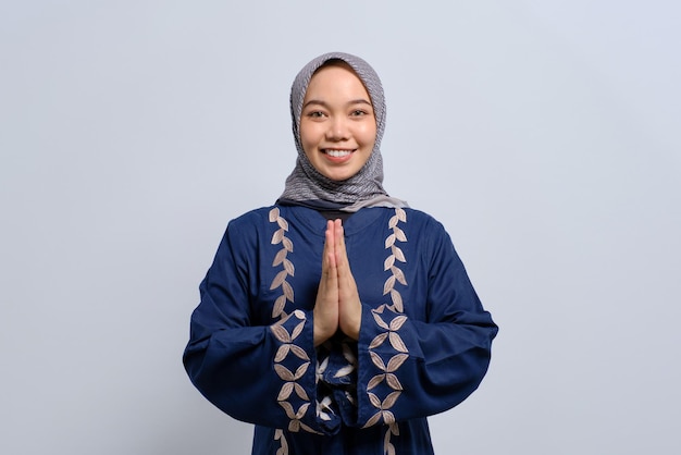 Sonriente joven musulmana asiática gesticulando Eid Mubarak saludo aislado sobre fondo blanco.