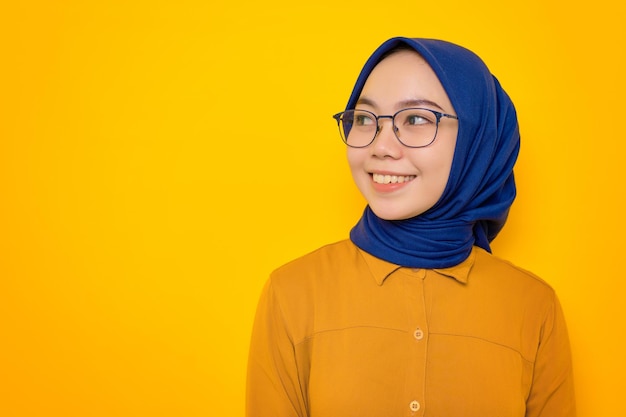 Sonriente joven musulmana asiática vestida con pantalones naranja mirando a la cámara con cara feliz aislada de fondo amarillo