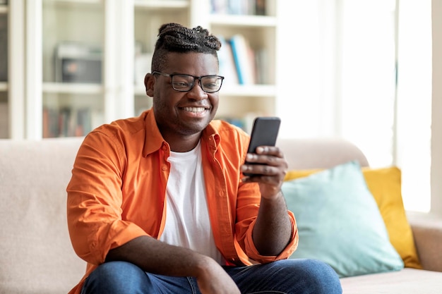 Sonriente joven negro con anteojos usando teléfono celular