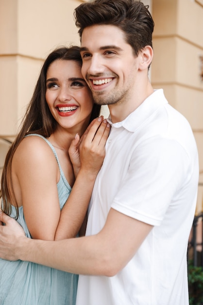 Sonriente joven pareja abrazándose en la calle de la ciudad, mirando a otro lado