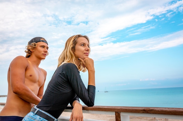 Sonriente joven pareja activa surfistas relajándose en la playa después del deporte.