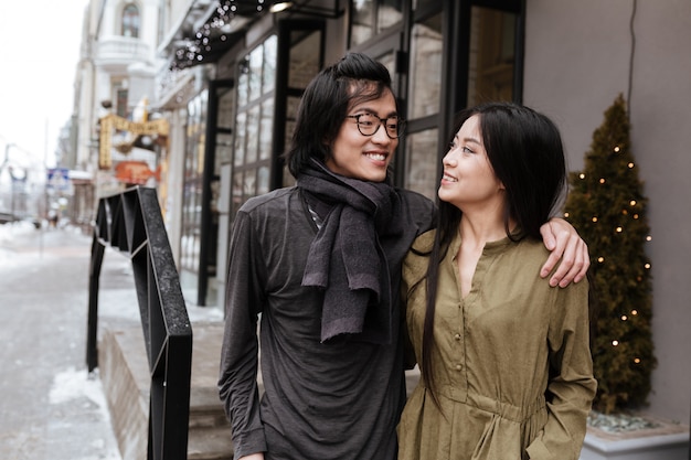 Sonriente joven pareja amorosa asiática de pie cerca del café al aire libre