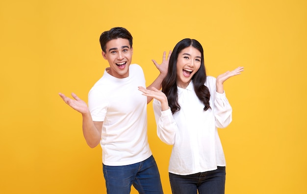 Sonriente joven pareja asiática hombre y mujer felices y asombrados sobre fondo amarillo.