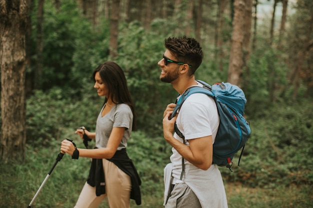 Sonriente joven pareja caminando con mochilas en el bosque