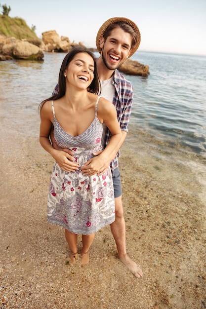 Sonriente joven pareja de enamorados de pie en la playa y abrazar