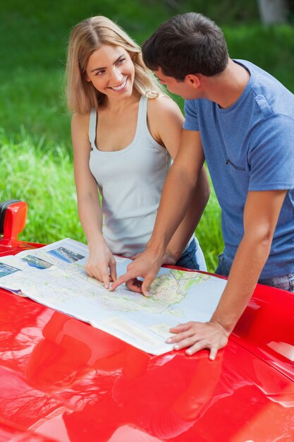 Sonriente joven pareja leyendo mapa en su capó cabriolet