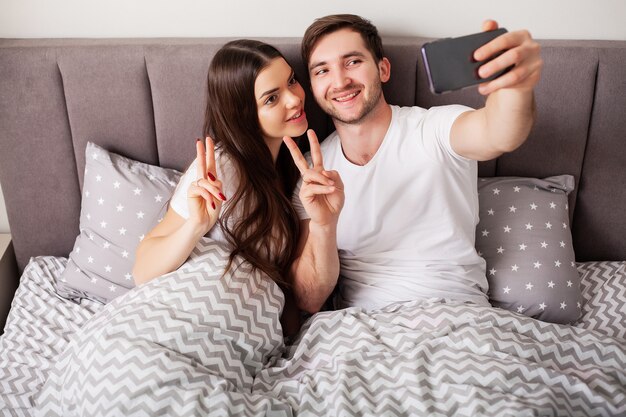 Sonriente joven pareja tomando selfie juntos en el dormitorio