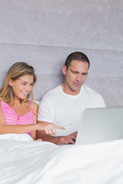 Sonriente joven pareja usando su computadora portátil juntos en la cama