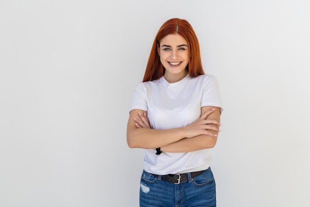 Sonriente joven pelirroja mujer sosteniendo las manos cruzadas, mirando a un lado posando aislado en blanco