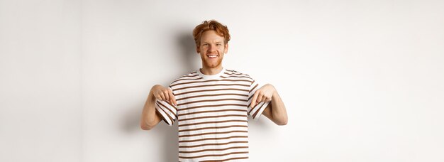 Sonriente joven con pelo rojo desordenado y barba apuntando con el dedo hacia abajo recomendando tienda de pie ove