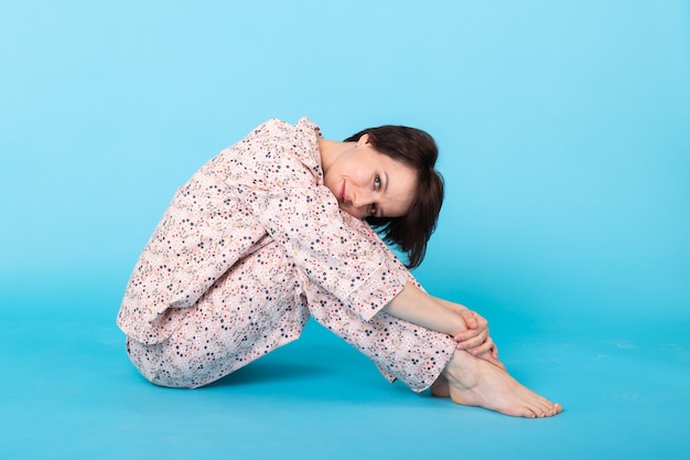 Sonriente joven en pijama ropa de casa posando mientras descansa en casa aislado en la pared azul