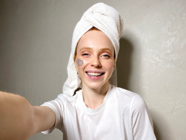 Sonriente joven pone una mascarilla cosmética en su rostro