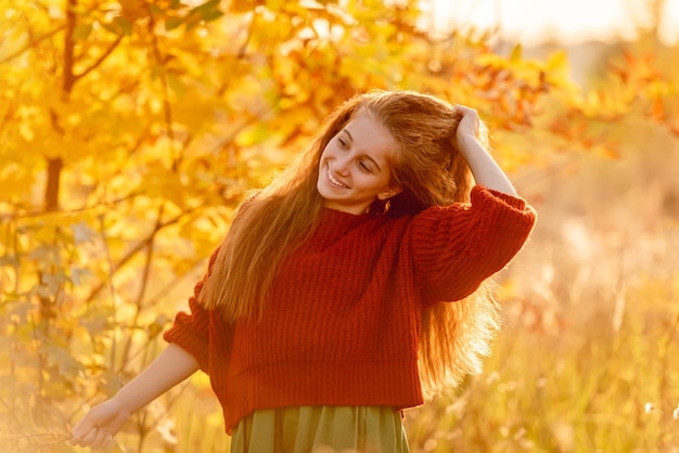 Sonriente joven posando cerca de otoño árbol amarillo en el parque soleado