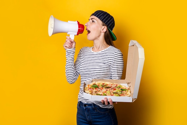 Sonriente joven repartidor de pizzas gritando por un megáfono mientras sostiene la pizza en amarillo