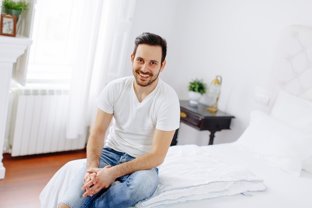 Sonriente joven sentado en la cama en el dormitorio en casa