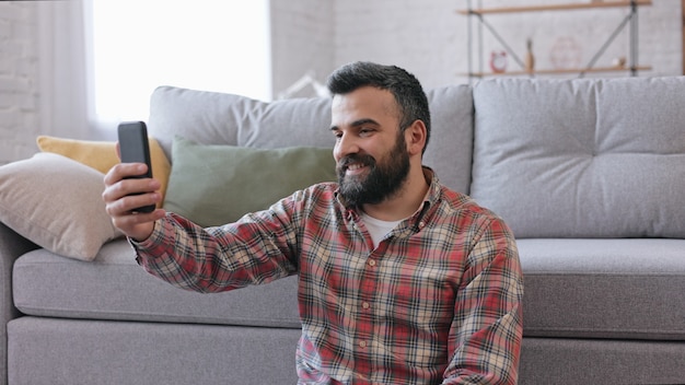 Sonriente joven con smartphone para reuniones en línea, videollamadas, videoconferencias.