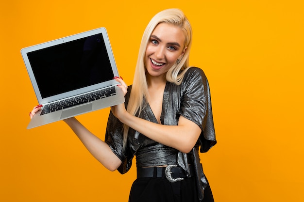sonriente joven sosteniendo una computadora portátil con una pantalla en blanco para insertar una página web en una superficie de estudio amarilla