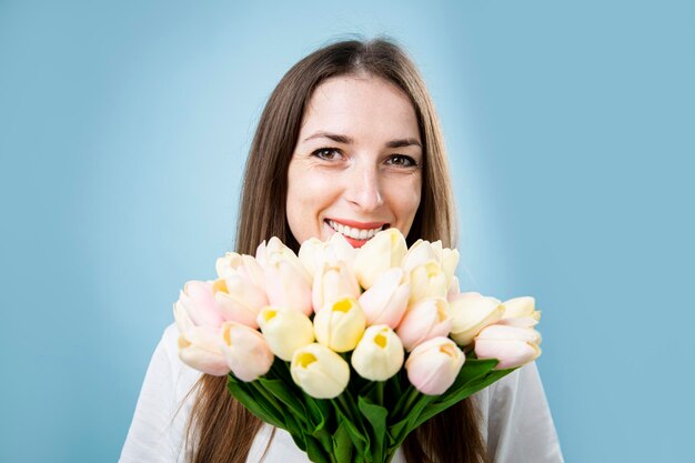 Sonriente joven sosteniendo ramo de tulipanes sobre fondo azul.