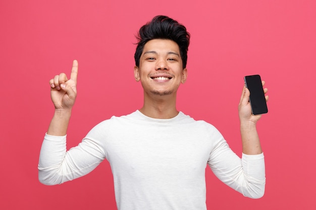 Sonriente joven sosteniendo teléfono móvil apuntando hacia arriba